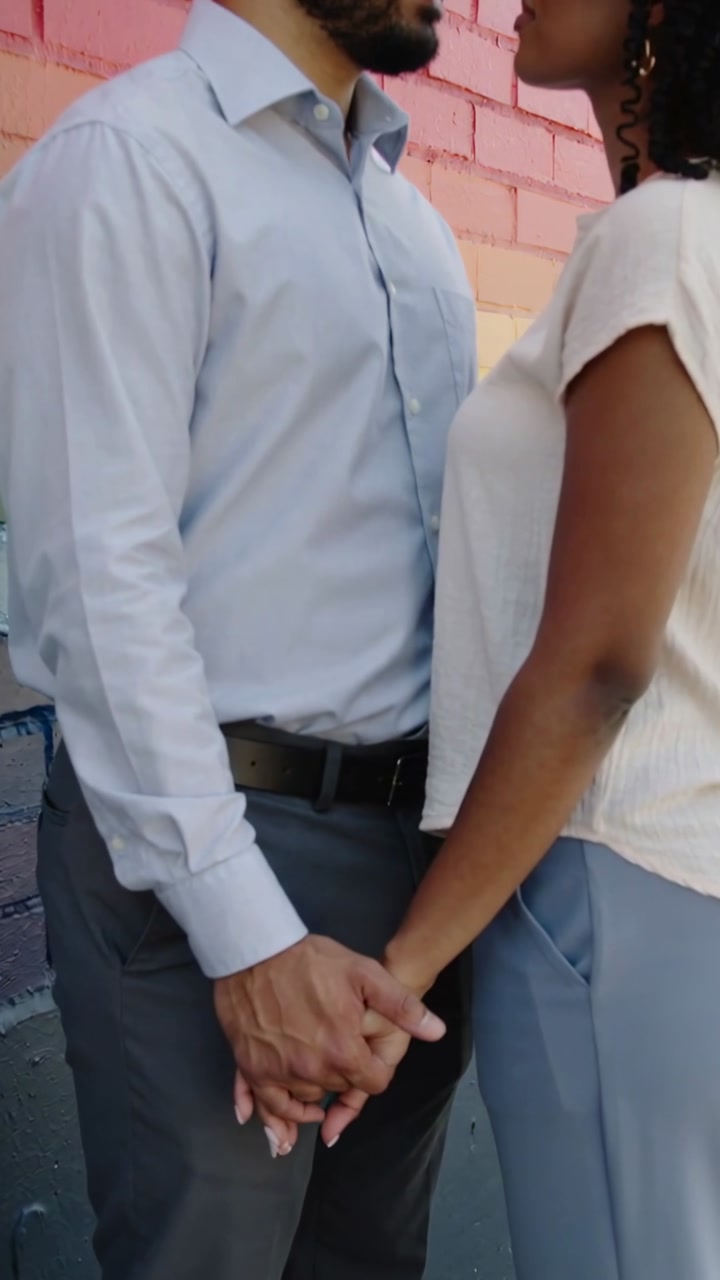 Vertical video: Holding hands, couple in blue shirt and blouse leaning toward kiss against mural