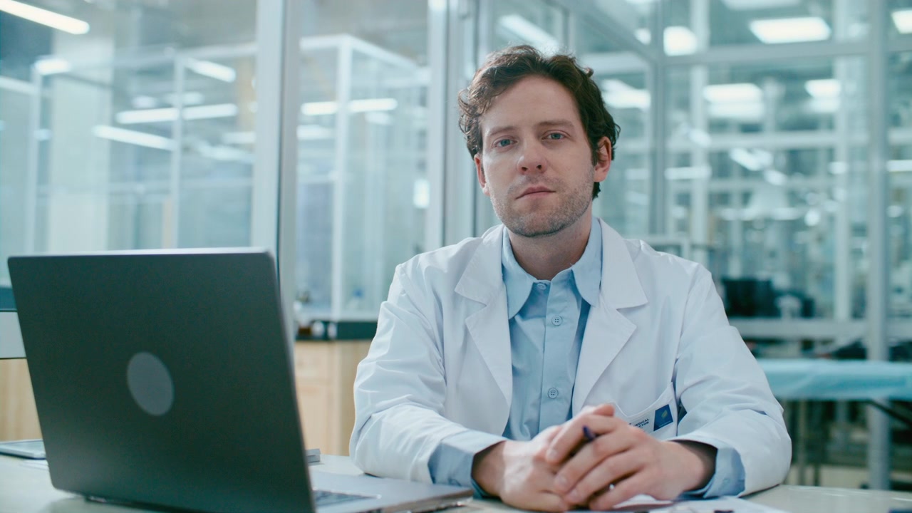 Portrait of Young Male Doctor Sitting at Desk with Laptop in Medical Office