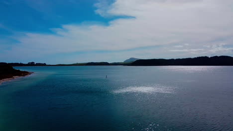 drone shot moving toward paddle boarder on a lake at kai iwi lake, new zealand