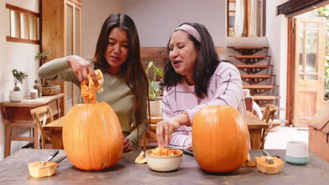 carving pumpkins, multiracial grandmother and young woman, at home, halloween time