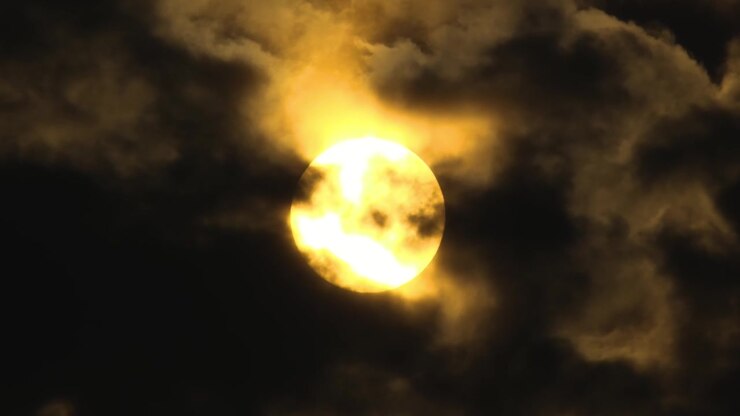 Fixed clip of dark gloomy clouds moving over sun with grey sky