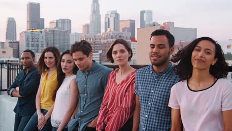 portrait of friends standing in a line gathered on rooftop terrace with city skyline in background