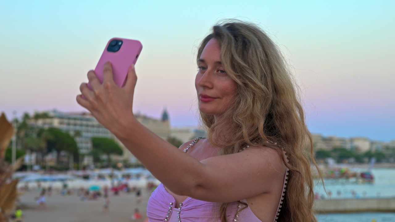 Donna con un vestito rosa che scatta foto sulla spiaggia di Cannes, in Francia, di sera