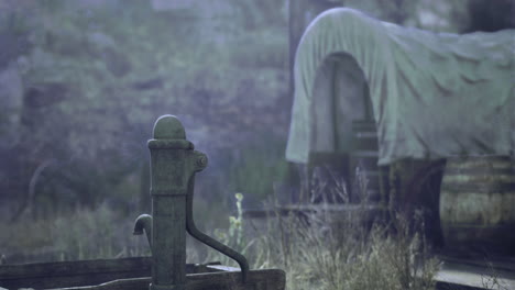 old water pump near covered wagon in a quiet rural setting at dusk