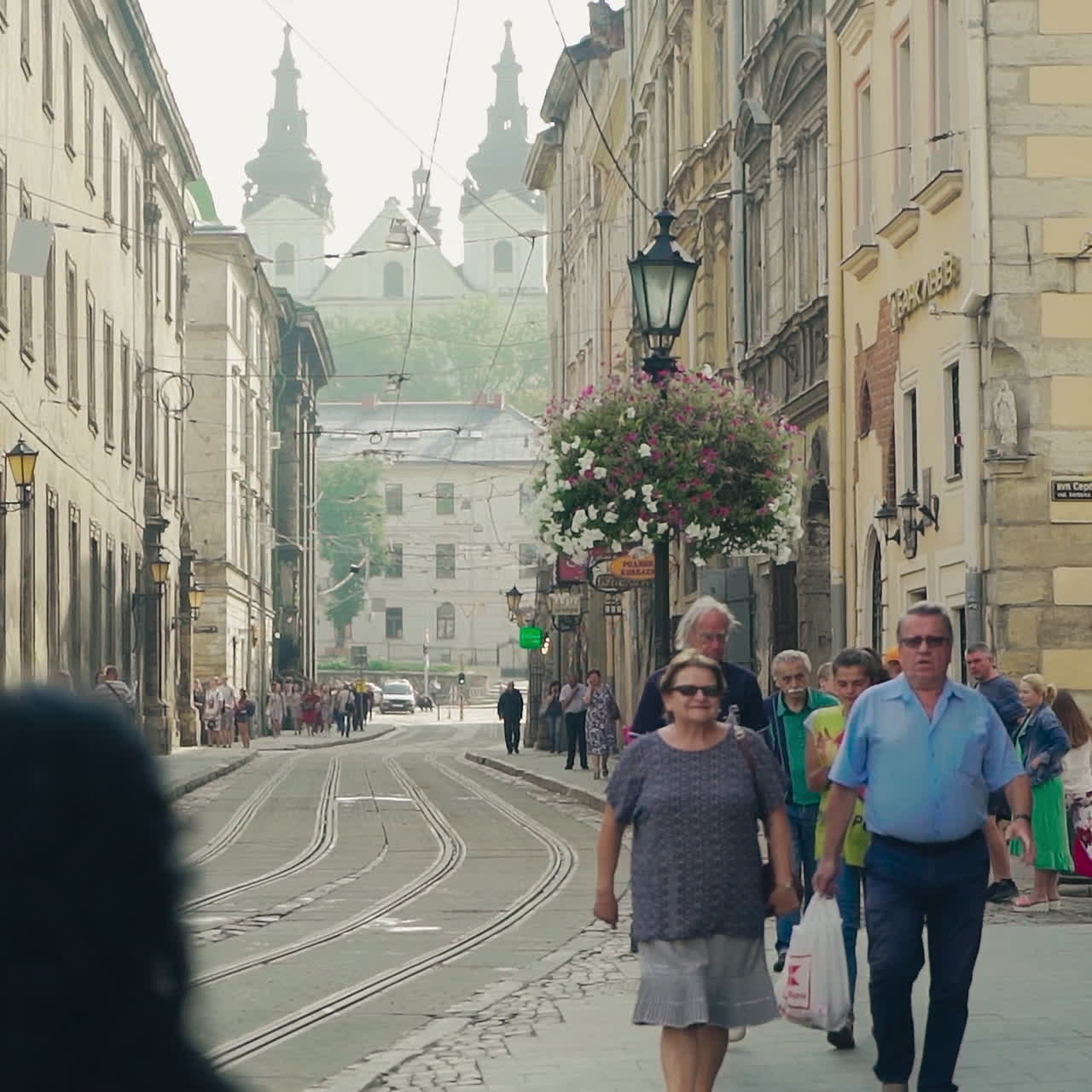 Central city street with ancient buildings and tourists walking on along. People go on the old pavement road in the historical city Lviv in summer. Slow motion