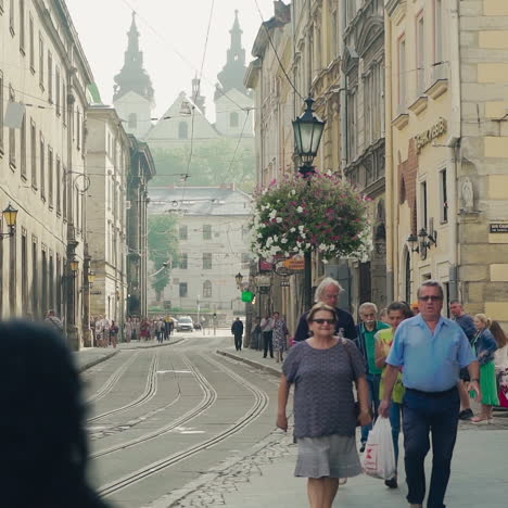 central city street with ancient buildings and tourists walking on along. people go on the old pavement road in the historical city lviv in summer. slow motion