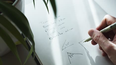 Close-up-shot-of-a-hand-trying-to-solve-a-geometry-problem-by-drawing-90-degree-angle-in-a-notebook-at-daytime