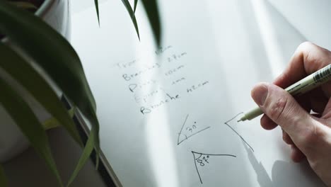 Close up shot of a hand trying to solve a geometry problem by drawing 90 degree angle in a notebook at daytime