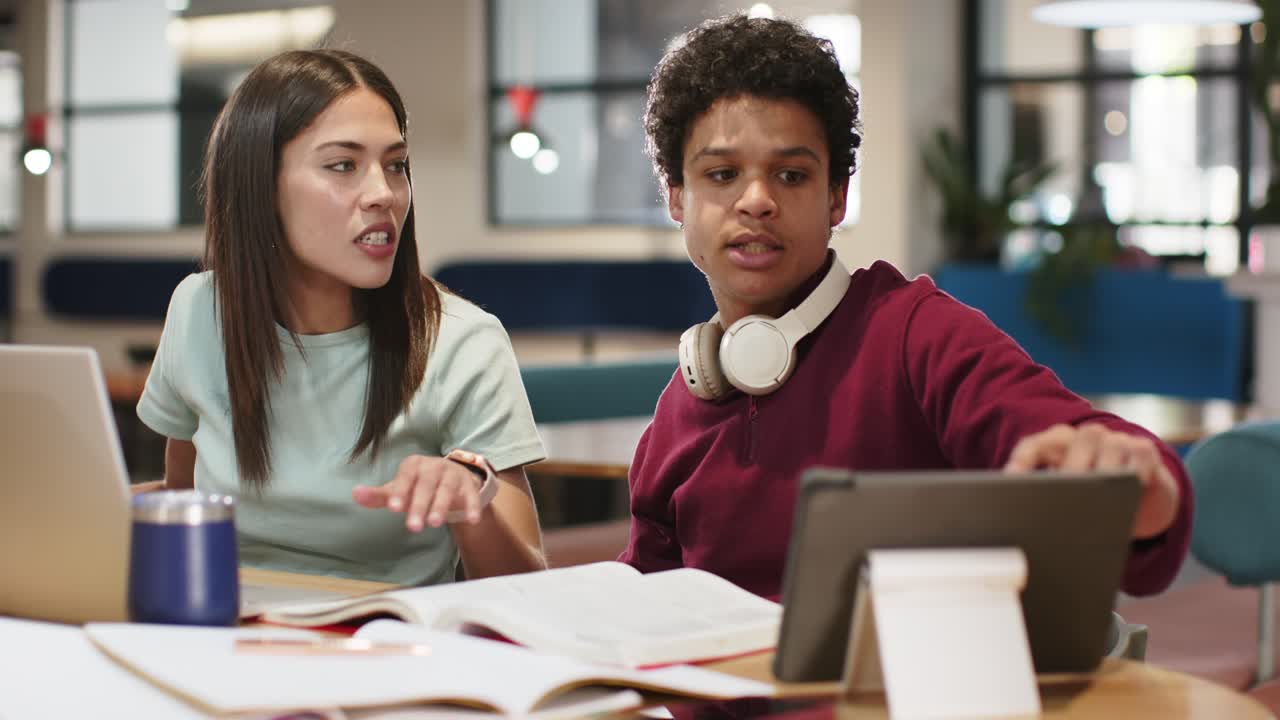 African American students at desk woman leaning, pointing at tablet man adjusting and studying book