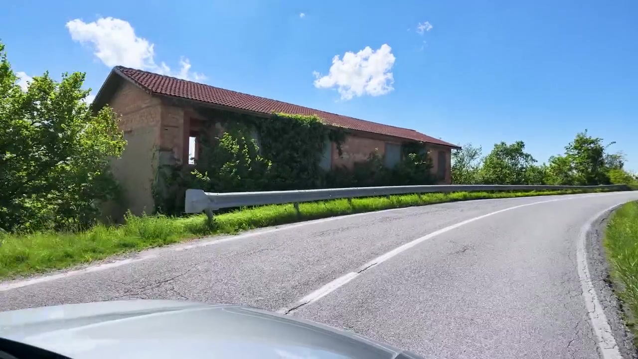 Et førstepersonskørselsperspektiv følger en snoet asfaltvej gennem solrige italienske landskabsbakker.