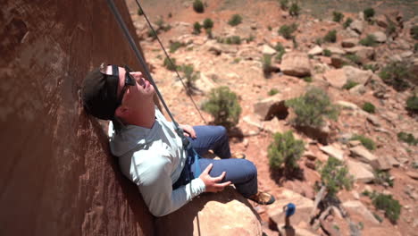 climber taking break, sitting on red stone cliff step on hot sunny day, slow motion