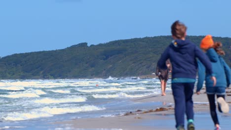 dos niños corriendo por la playa en un día ventoso con una colina forestal en la parte de atrás