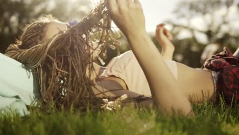 Trendiges-Hipster-Mädchen-Mit-Dreadlocks,-Das-Sich-Auf-Dem-Gras-Im-Park-Entspannt.-Sommer-Lifestyle-Porträt-Einer-Hipster-Frau,-Die-Auf-Dem-Gras-Liegt