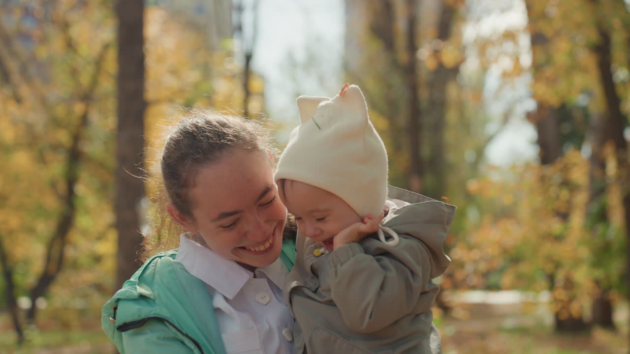 Tenero abbraccio familiare. Madre gioiosa che tiene in braccio un neonato sorridente. Scena nel parco illuminata dal sole con madre e figlio affettuosi. Un momento luminoso e allegro di una madre che coccola il suo bambino gioioso all'aperto.