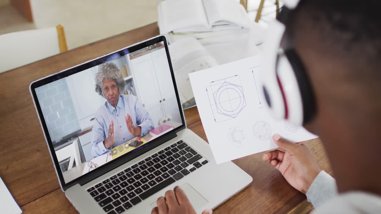 Afroamerikanischer Student hält Notizen während eines Videoanrufs am Laptop zu Hause