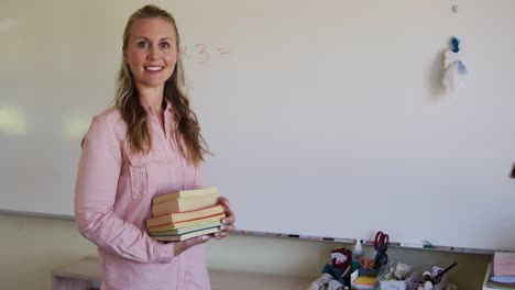 Female-teacher-holding-stack-of-books-in-school