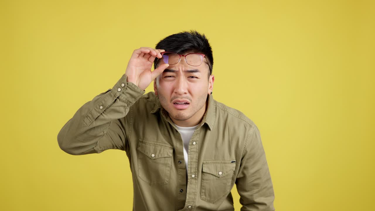 Young Asian Man Squinting and Adjusting Glasses with a Confused Expression