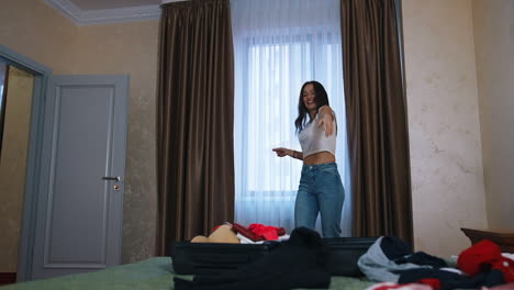 cheerful woman packing suitcase. happy girl dancing and putting stuff into a luggage before a journey. beautiful woman in comfortable room hotel.