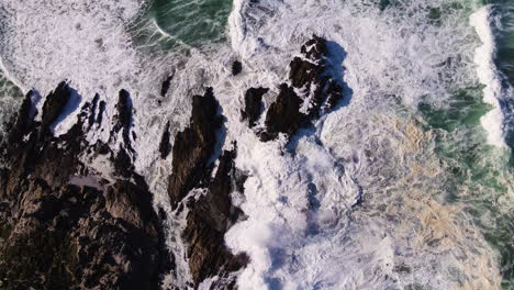 aerial riser above waves crashing spectacularly against jagged coastline