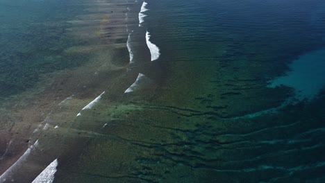 spur and groove reef flats in clear ocean water as waves crest and break in shallows, aerial overview