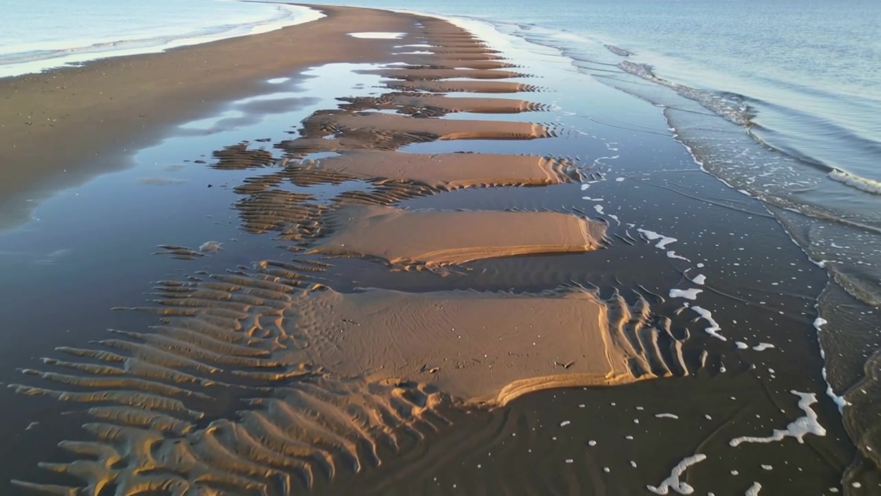 Moving camera revealing sand terraces at spit, showing tidal pools and foam lines showing pattern