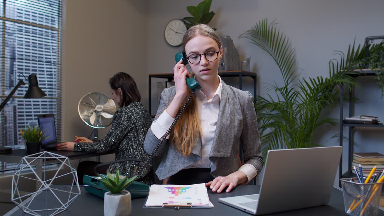 Portrait of business woman looking camera doing gesture call me back with retro telephone at office