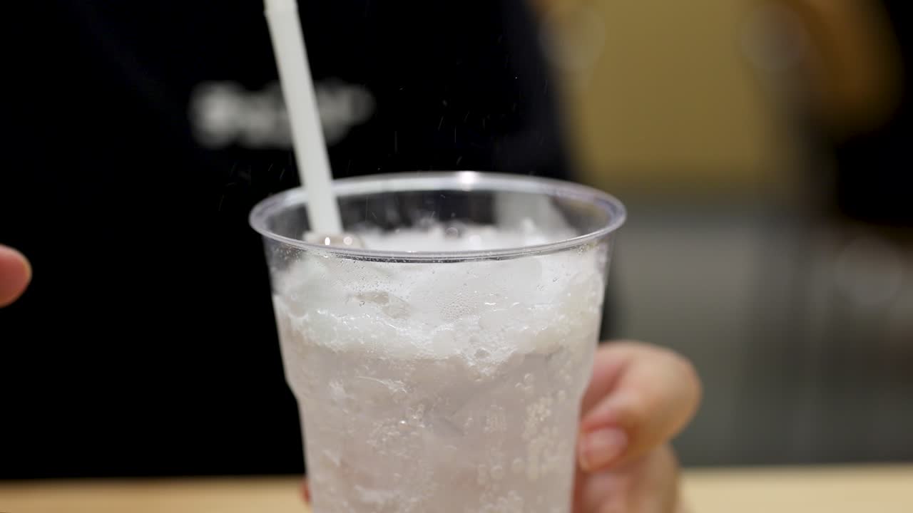 Hand pours carbonated drink over ice, bubbles rising, in bright indoor setting, close-up view