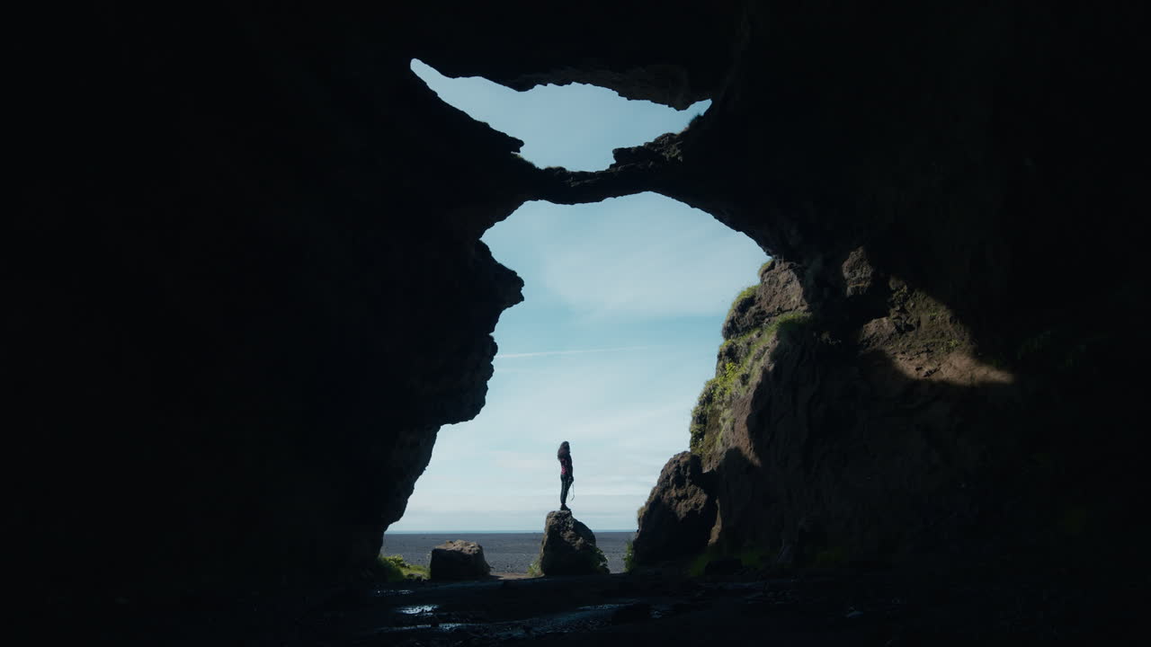 Wide angle shot from inside Yoda Cave, Iceland, woman taking picture, moody silhouette 01