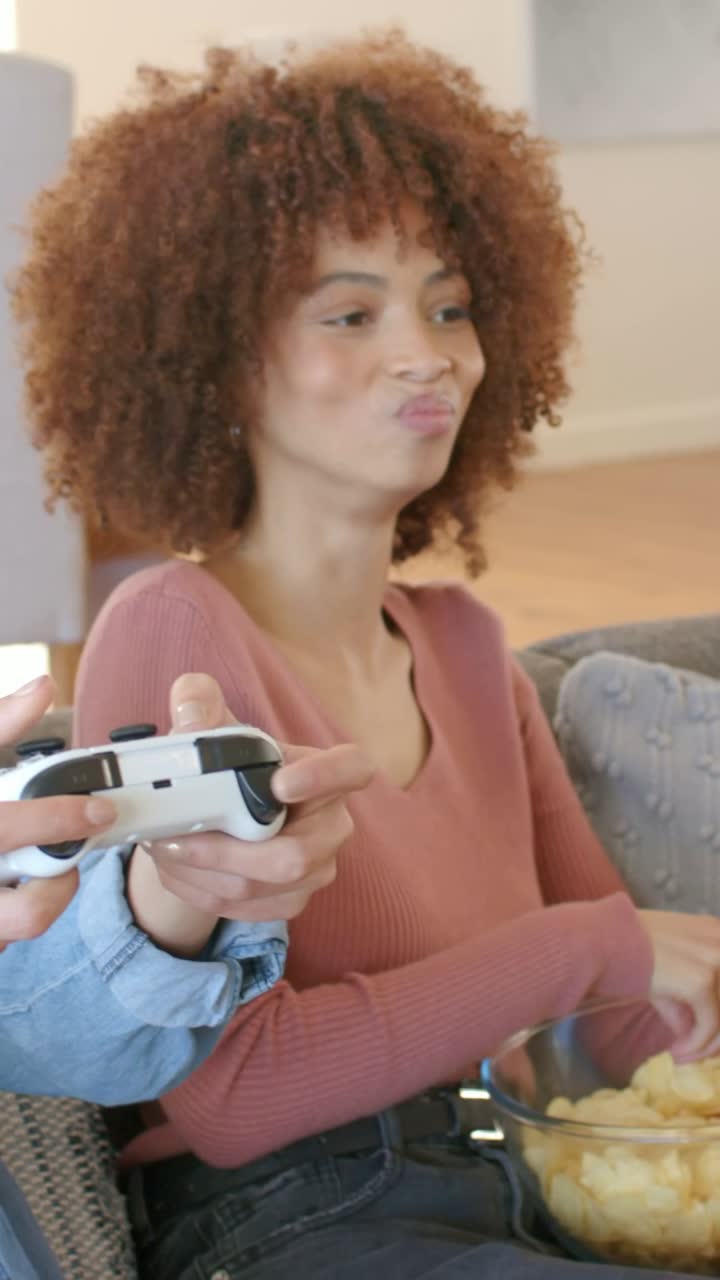 Vertical video: Watching woman in pink sweater reaching for chip bowl on couch, controller moving