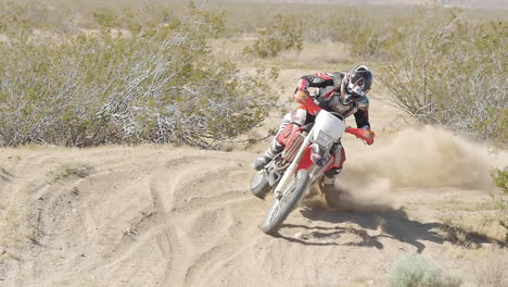 slow motion: a dirt biker rides his crf honda through the desert and whips around a berm