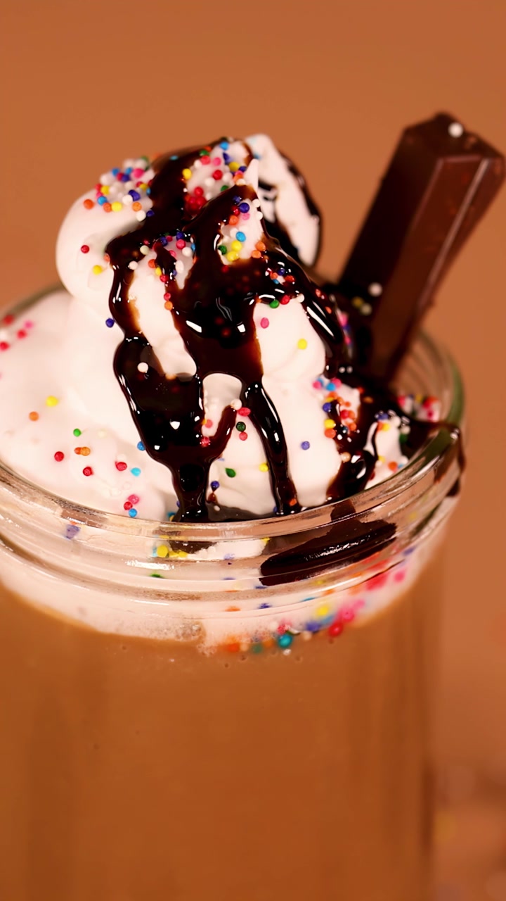 Lento movimento verticale della telecamera su un cremoso milkshake al cioccolato guarnito con panna montata, sciroppo e codette di zucchero