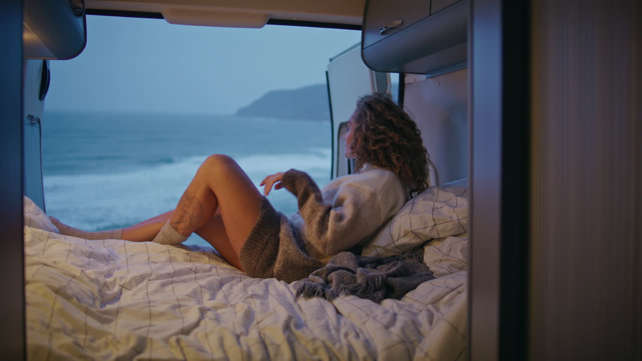 mujer relajante acogedora caravana mirando sombrío paisaje marítimo de la noche. mujer tranquila mintiendo