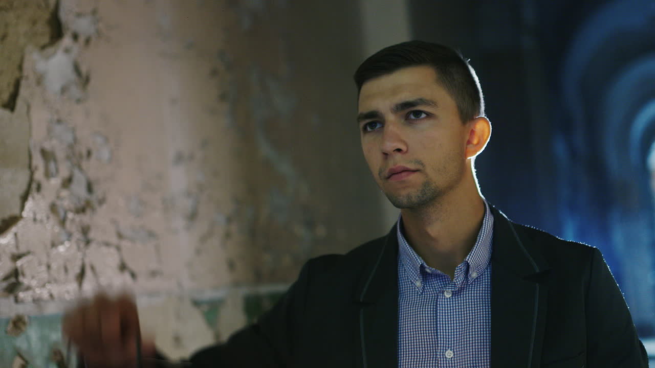 joven asustado en un pasillo oscuro sosteniendo una lámpara de aceite en la mano vestido con traje