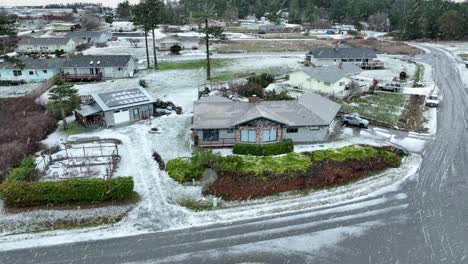 aerial view of a snow falling on a rural house with a solar panel covered out building