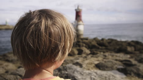 young boy looking at a lighthouse at the beach