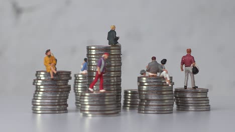 miniature people standing on piles of different heights of coins.