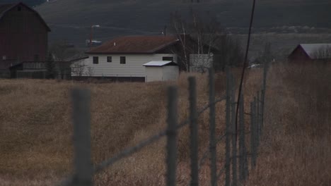 The-Camera-Looks-Over-A-Fence-To-A-Rural-Farm-In-Early-Winter