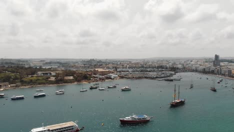 aerial 4k drone footage panning from a harbor with anchored sea vessels and revealing a cityscape of the mediterranean island town of sliema, malta