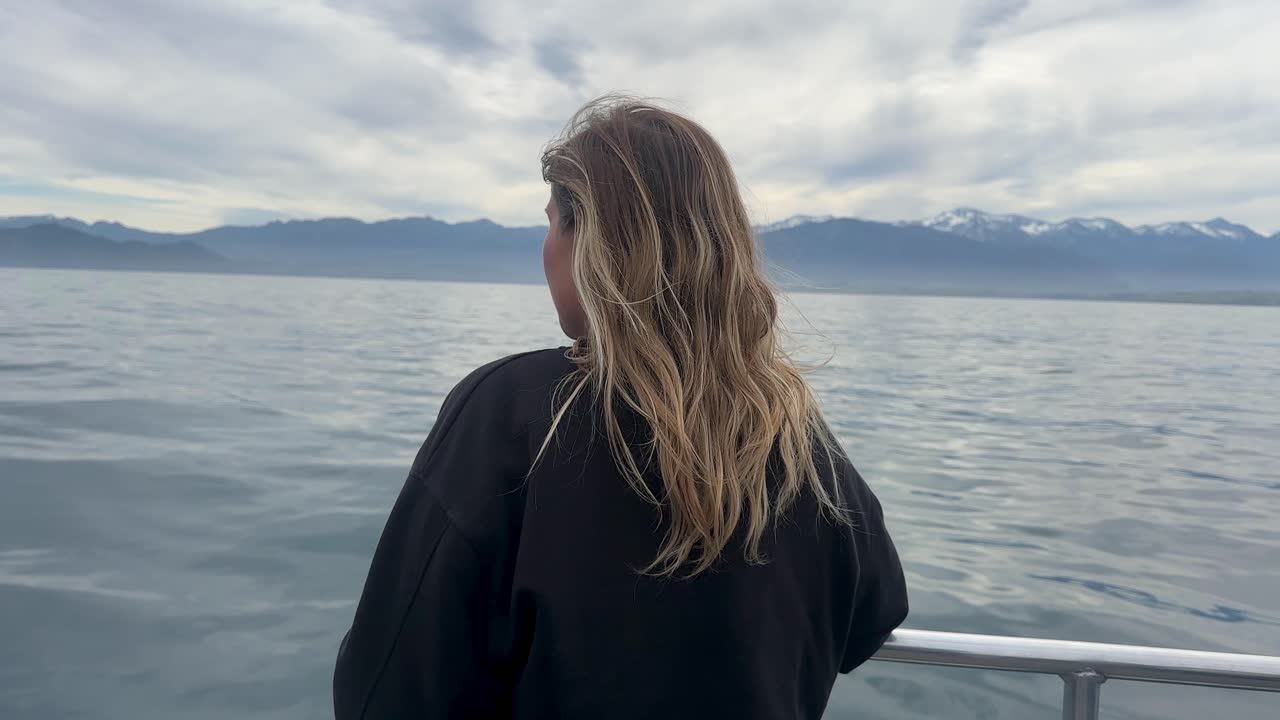 A woman stands at the front of a boat on a whale watching tour from Kaikoura, New Zealand. Ocean views, marine life, and dramatic coastal scenery create an unforgettable experience