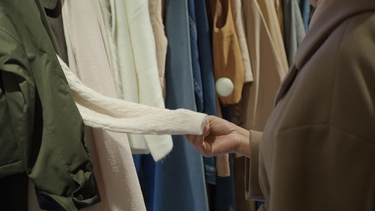 店内でラックにかかった服を見て触れる女性