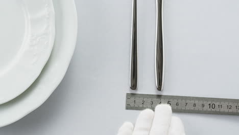 professional table setting with white gloves. plates, fork, knife, and glass arranged on a white table.