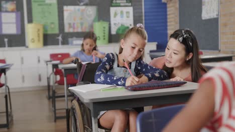 Happy-diverse-female-teacher-talking-to-girl-in-wheelchair-in-elementary-school-class,-slow-motion