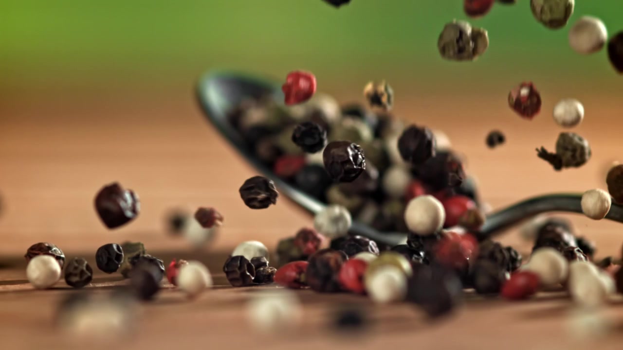 Mixed Peppercorns Falling onto a Spoon in Super Slow Motion