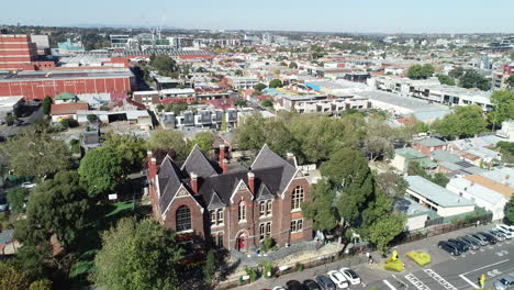 drone orbit of school with construction onsite revealing dense suburbs around with housing and industrial areas as well as green space adjacent