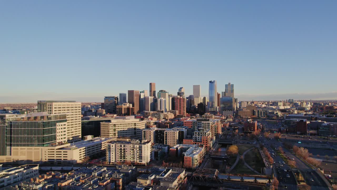 Vista aerea con drone dello skyline di Denver Colorado, mentre si allontana superando il complesso di appartamenti moderni e grattacieli The Confluence, durante il tramonto nell'ora d'oro.