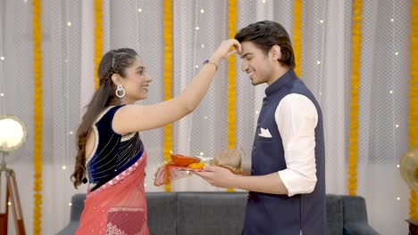 mujer india poniendo tilak en la frente de su pareja