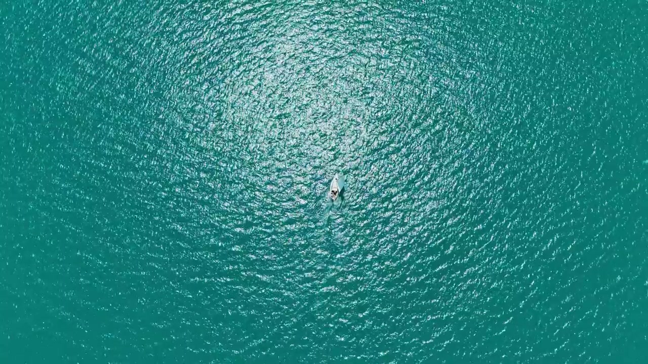 Sailboat glides over calm turquoise waters in bright sunlight on a clear day