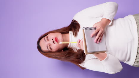 vertical of asian secretary businesswoman holding a notebook and thinking with list inspiration strategy for success on purple background-2