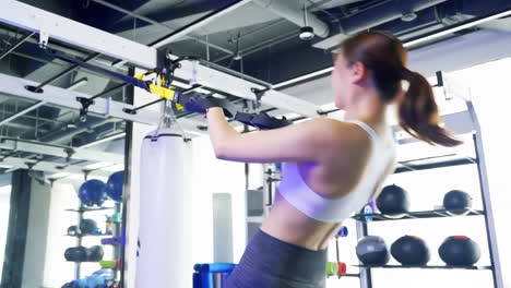 Athletic-muscular-fitness-woman-showing-suspension-training,-performing-pull-ups-exercise-with-trx-straps-at-gym