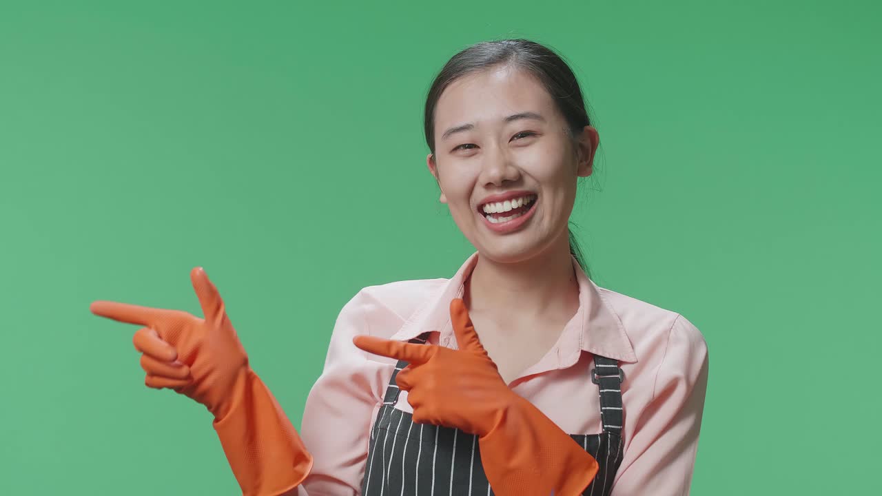 초록색 스크린 스튜디오에 서 있는 동안 미소 짓고 을 가리키는 아시안 여성 집주인의 클로즈업